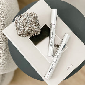 2 silver refillable mascars sitting on a beautiful book on a table